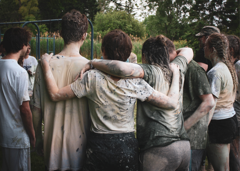 youth linked arm in arm after playing a muddy game.