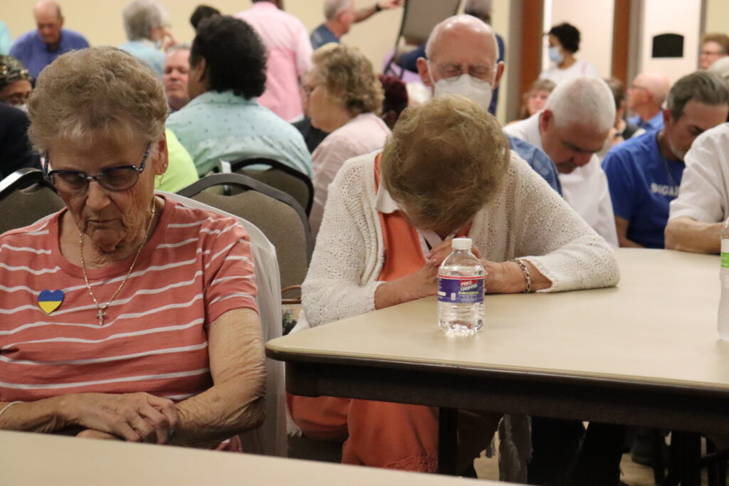 Older women bow their heads in prayer at the pastoral plan meeting.