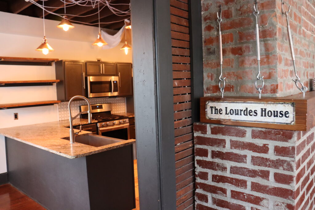 The Lourdes House at UCM Newman Center--a photo from the entryway with 'the Lourdes House' sign in the foreground, and the kitchen in the background.