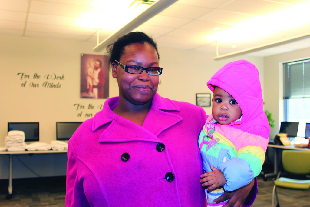 A mother in a pink jacket holds her young daughter in Catholic Charities' welcome center.